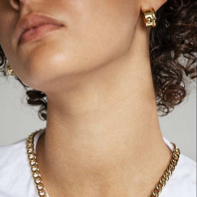 Close-up of a person wearing a gold necklace and earrings on a white background