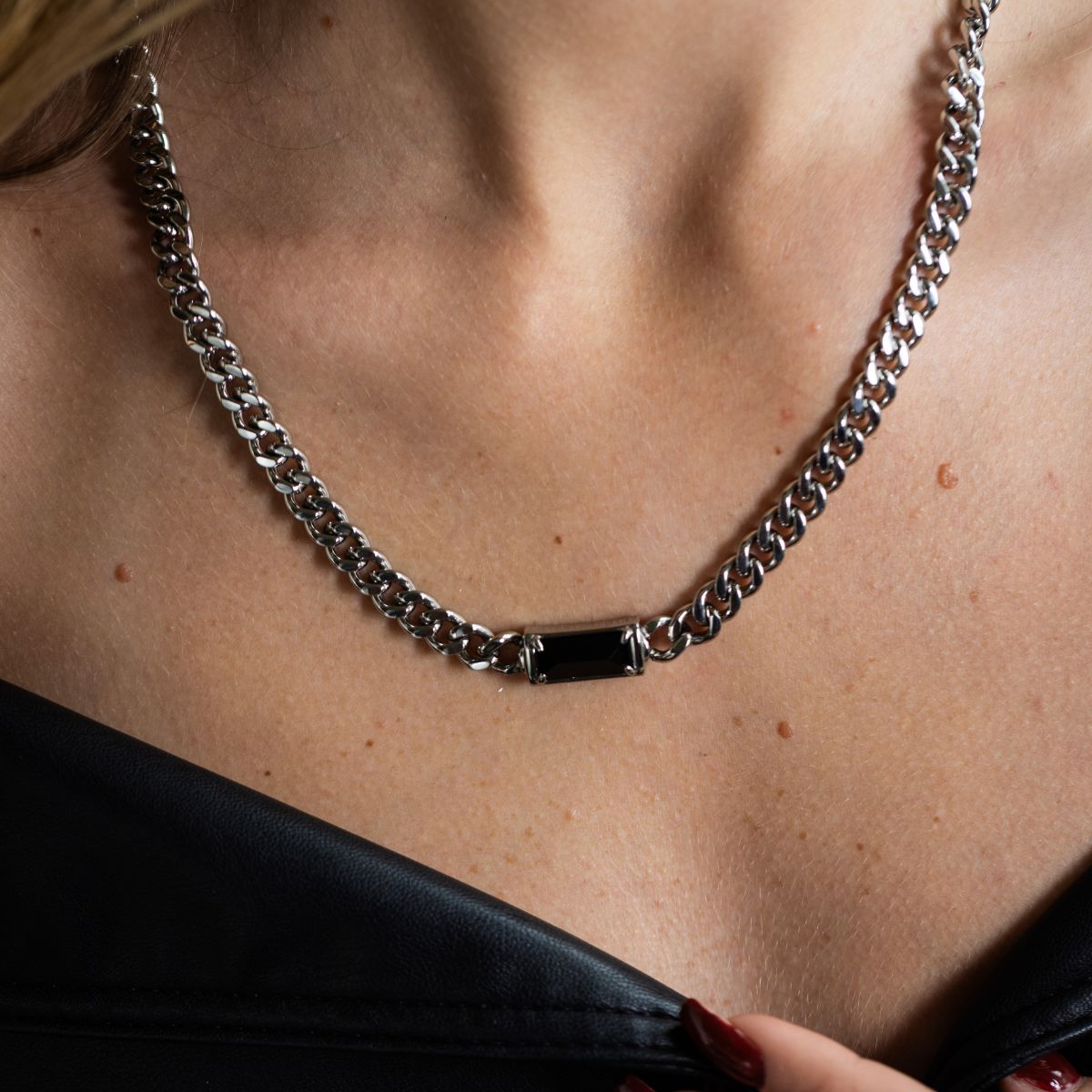 A close-up of a model wearing a silver-toned chain necklace with a rectangular black inlay at the center, paired with a black top.