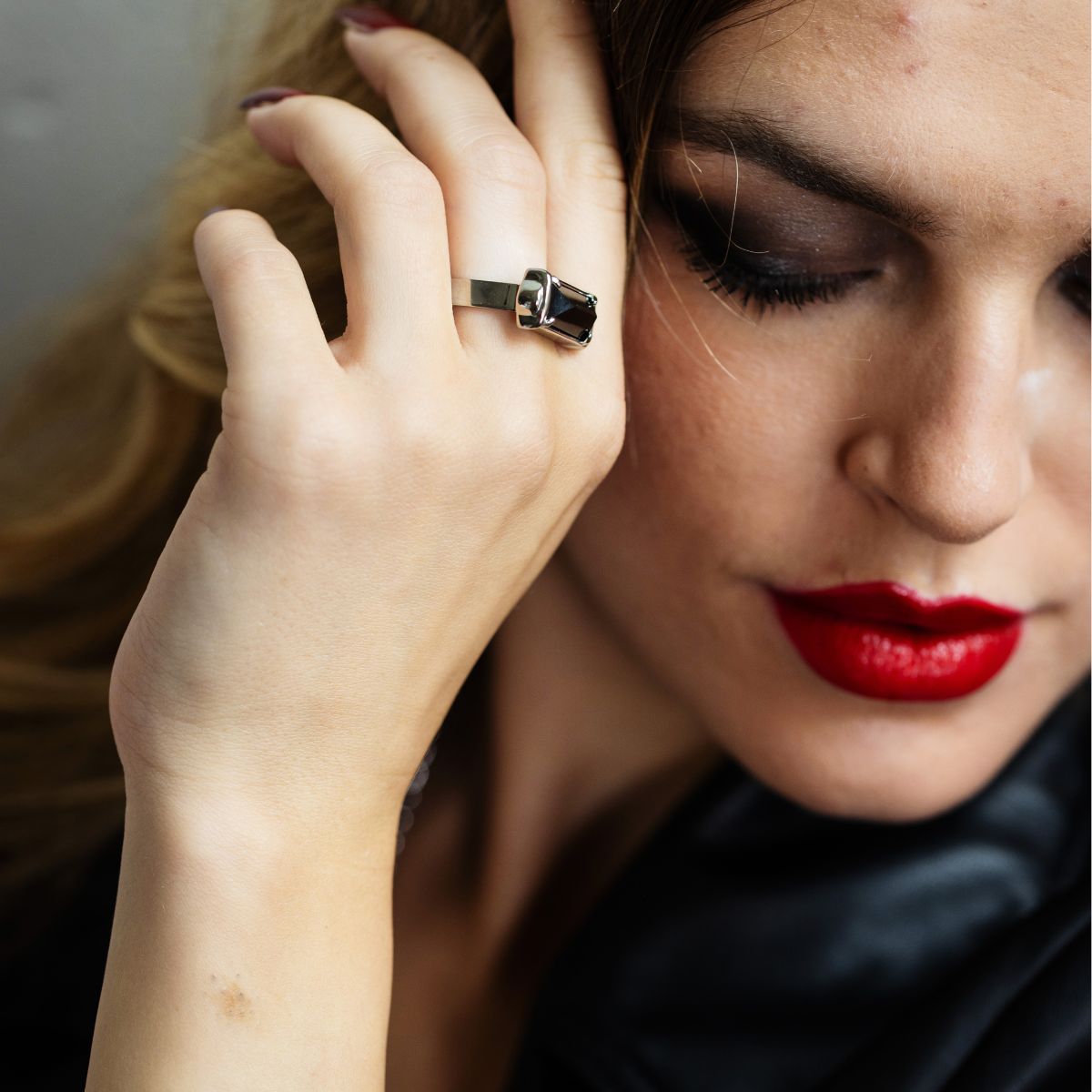 A close-up lifestyle shot of a woman wearing a silver ring with a black rectangular stone on her finger, with her hand resting near her face.