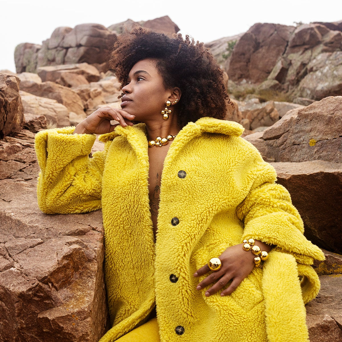 Woman in a bright yellow coat sitting on rocks in a natural setting
