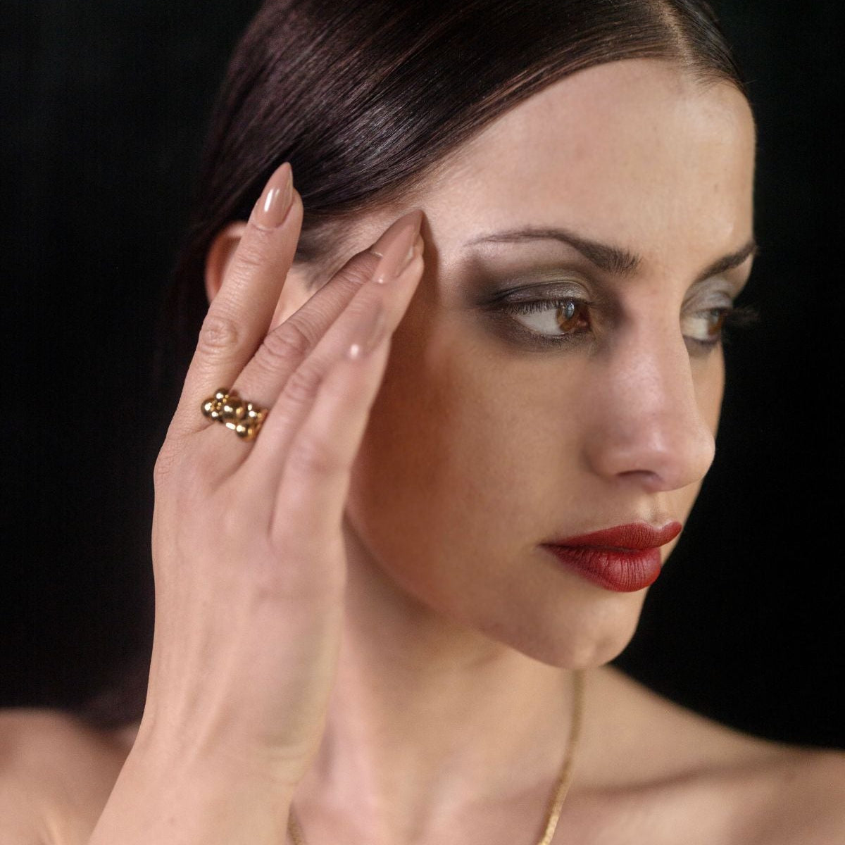 Woman wearing a gold necklace and earrings against a dark background