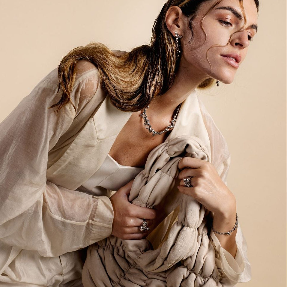Woman in a white outfit holding a beige fabric against a beige background