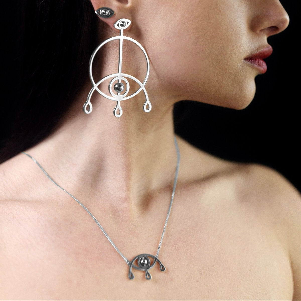 Woman wearing silver earrings and necklace with a dark background