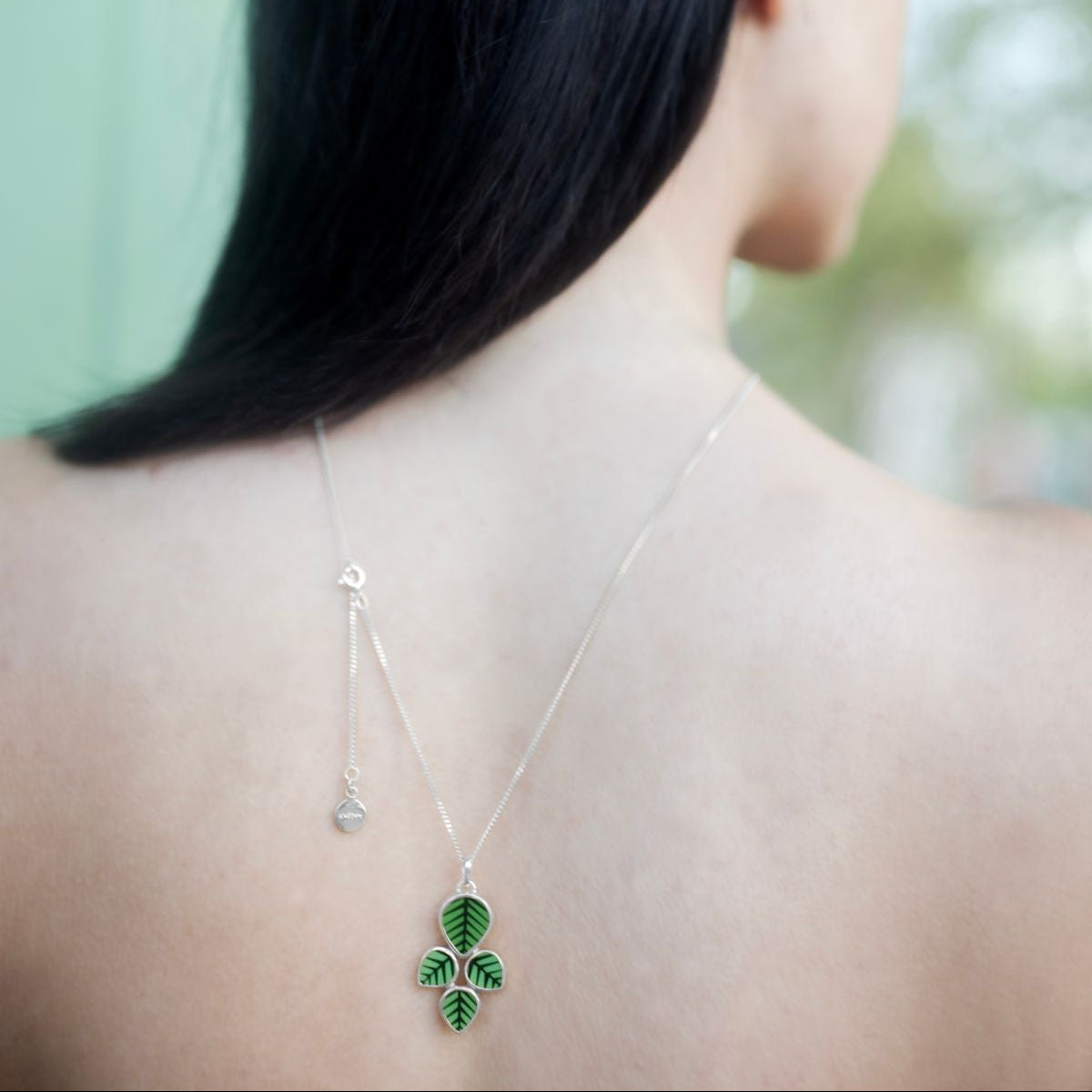 Person wearing a necklace with a green pendant on a blurred background