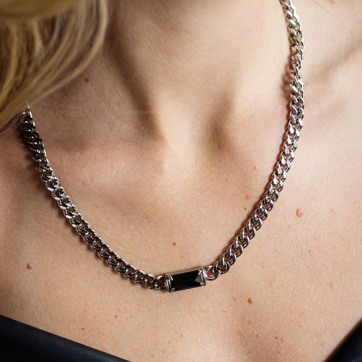 A close-up of a silver-toned chain necklace with a rectangular black inlay, worn on a person's neck.
