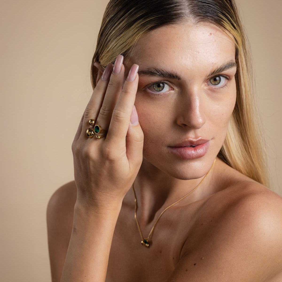 Woman with a gold ring on her finger against a beige background