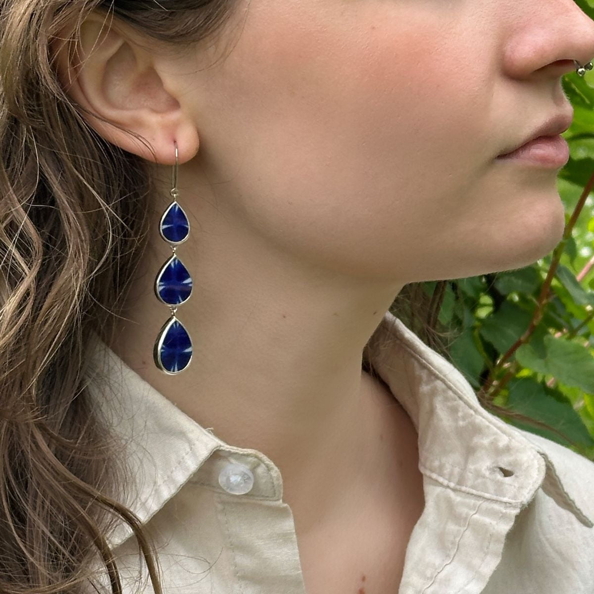 Woman wearing blue teardrop earrings with greenery in the background