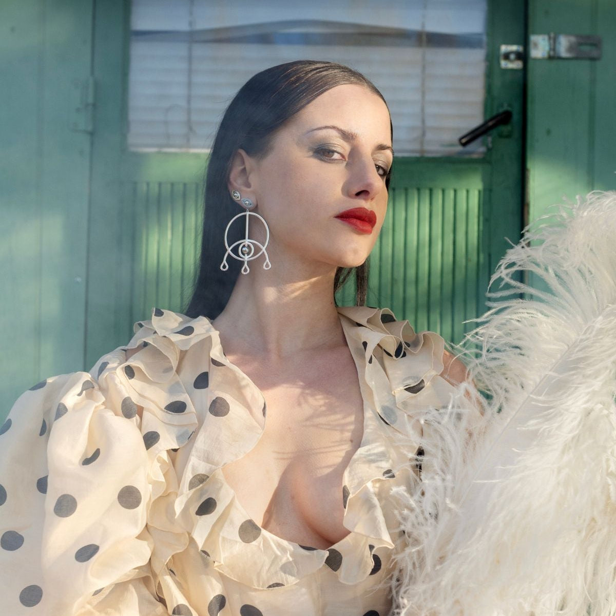 Woman wearing a polka dot blouse with a feathered garment in front of a green door.