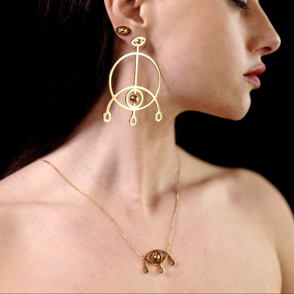 Woman wearing gold hoop earrings and necklace against a dark background